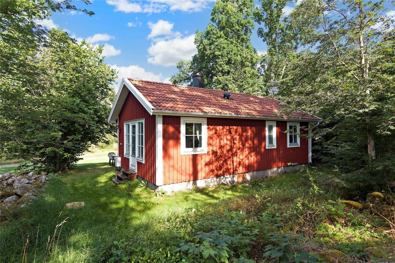 Red wooden house with white windows and roof surrounded by trees.