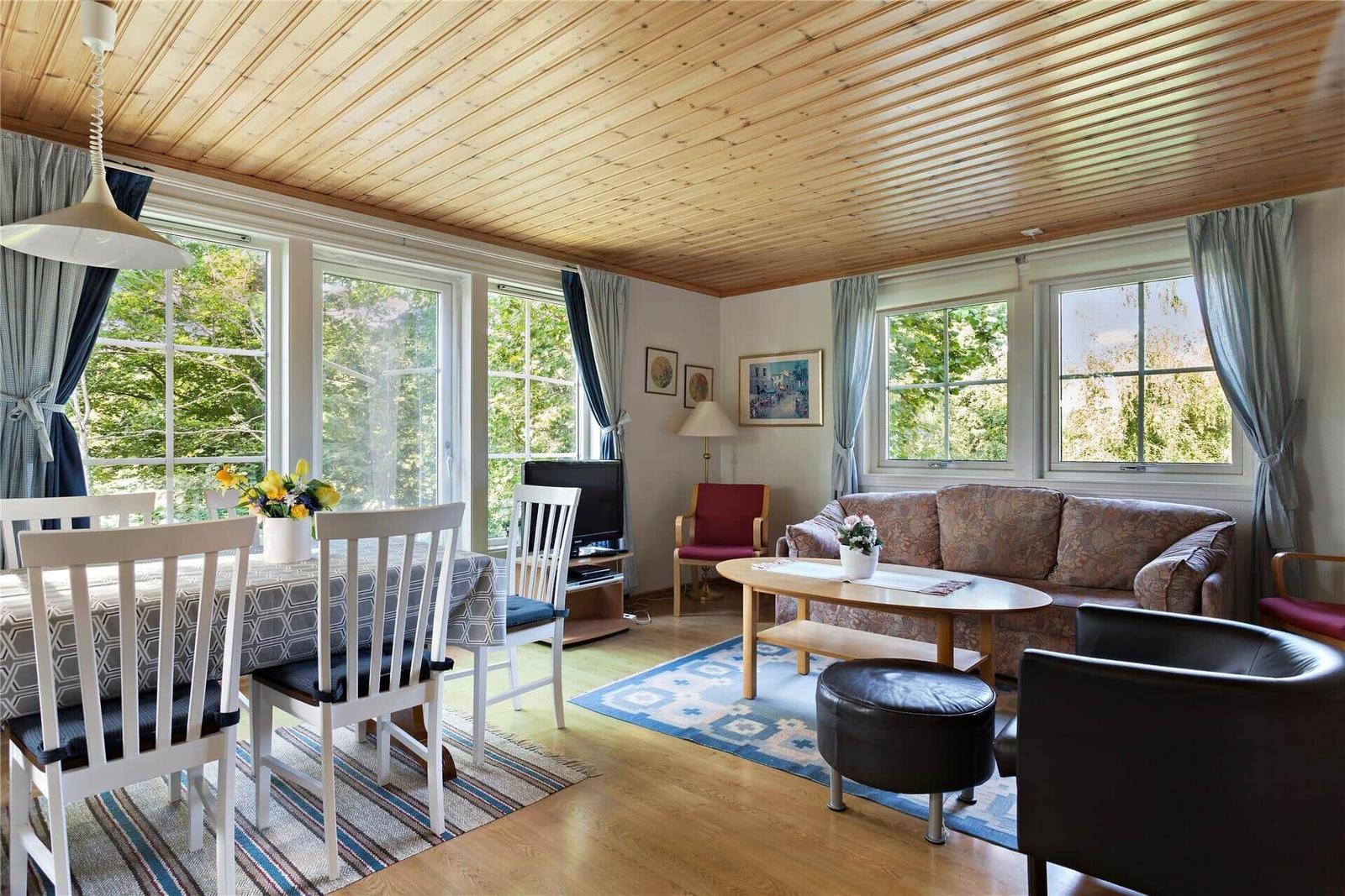Living and dining area with wooden ceiling, windows, and furniture.