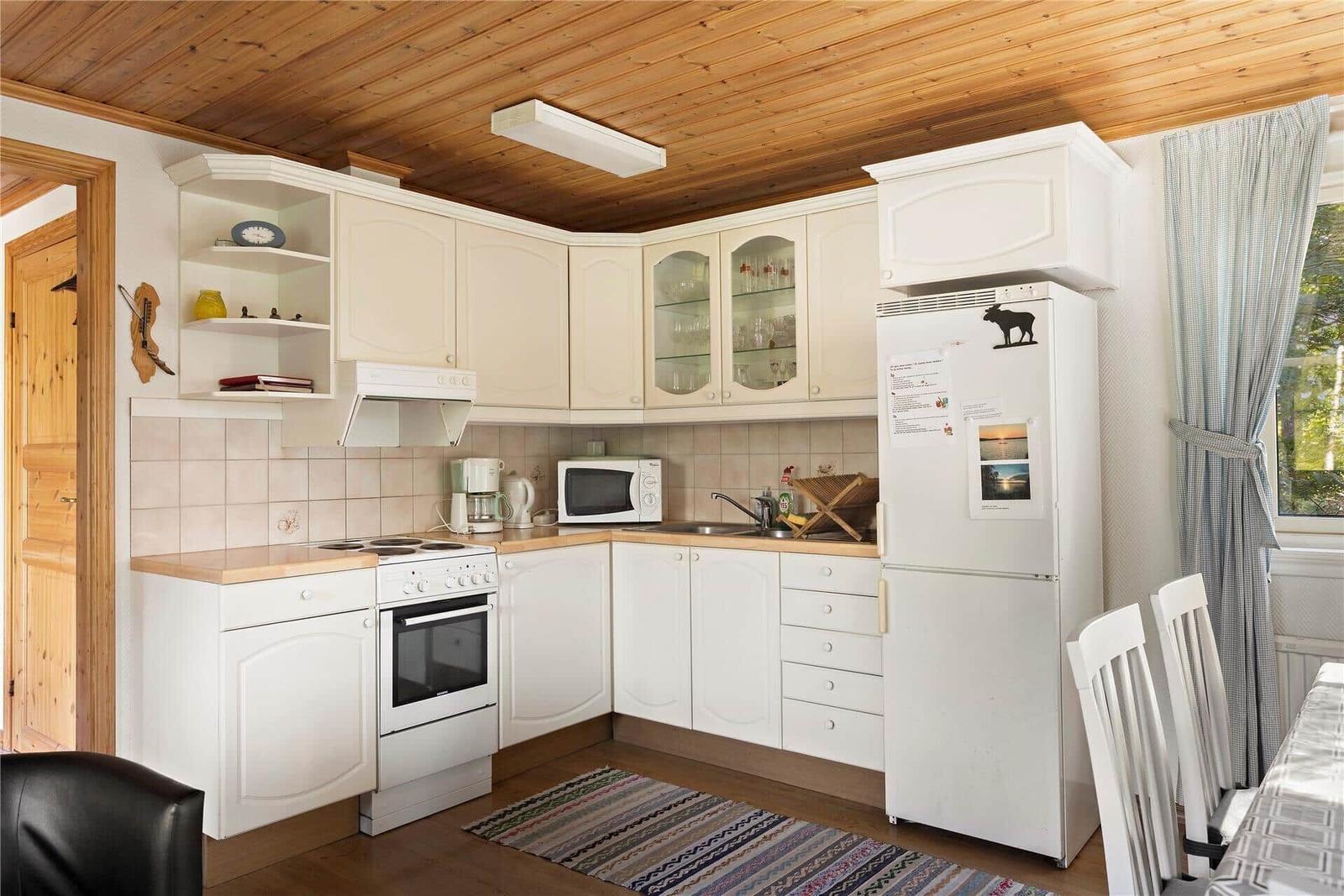 Kitchen with white cabinets, refrigerator, and window with curtains.