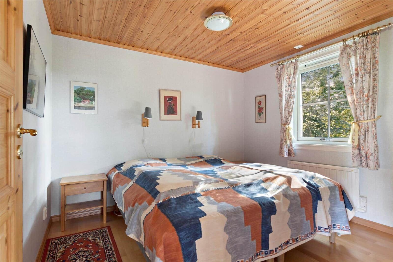 Bedroom with wooden ceiling, bed, and window with curtains.