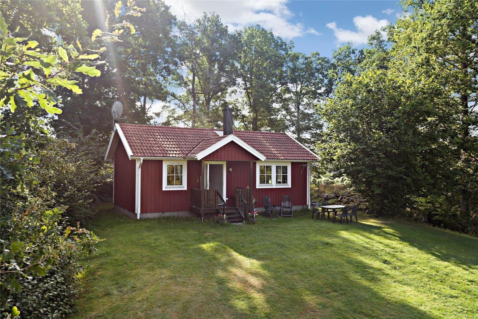 Red vacation house with terrace and garden in green surroundings.