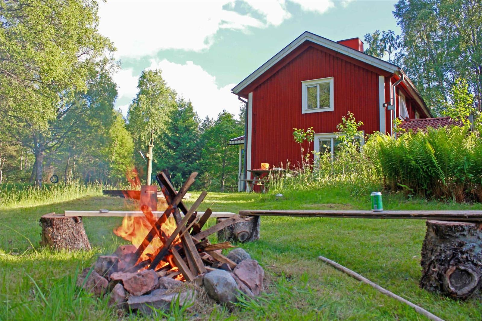 Red wooden house with grill area and campfire in the garden.