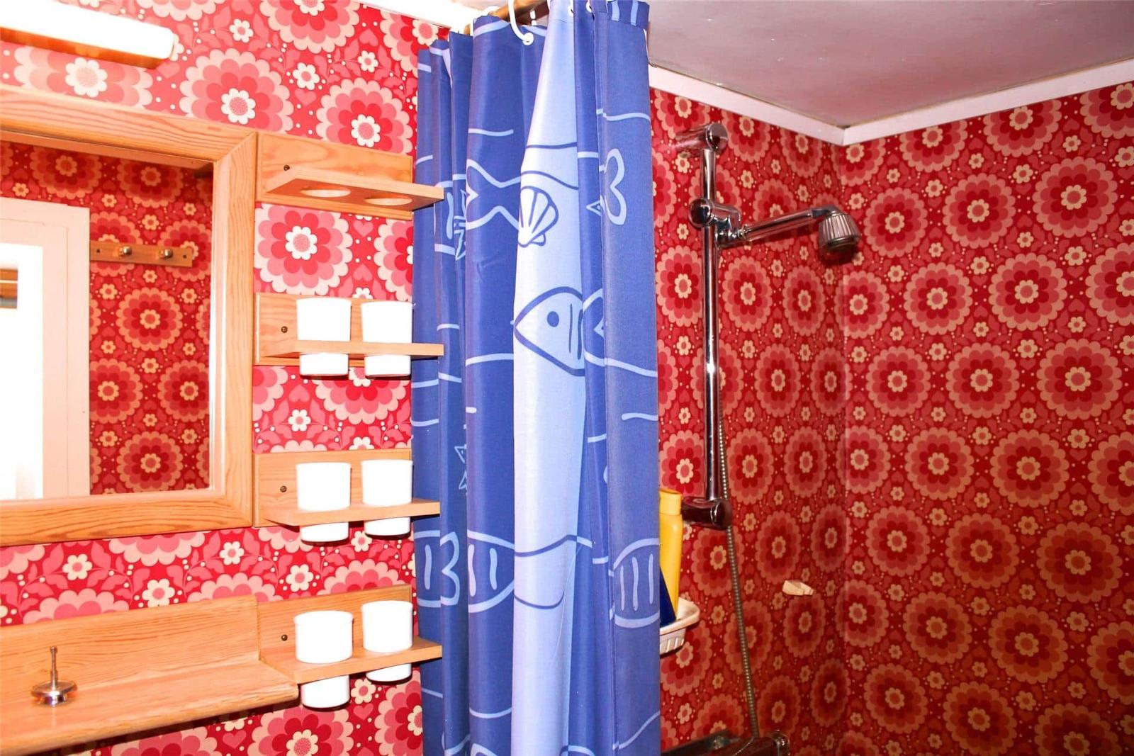 Bathroom with floral wallpaper, blue shower curtain, and wooden shelves.