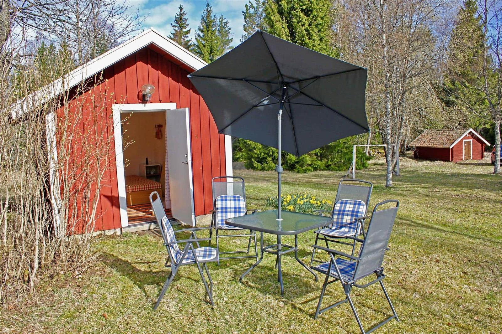 Red wooden cabin with patio, table, four chairs, and umbrella.