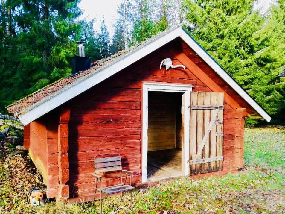 Red wooden house with open door and chair in front. Trees in the background.