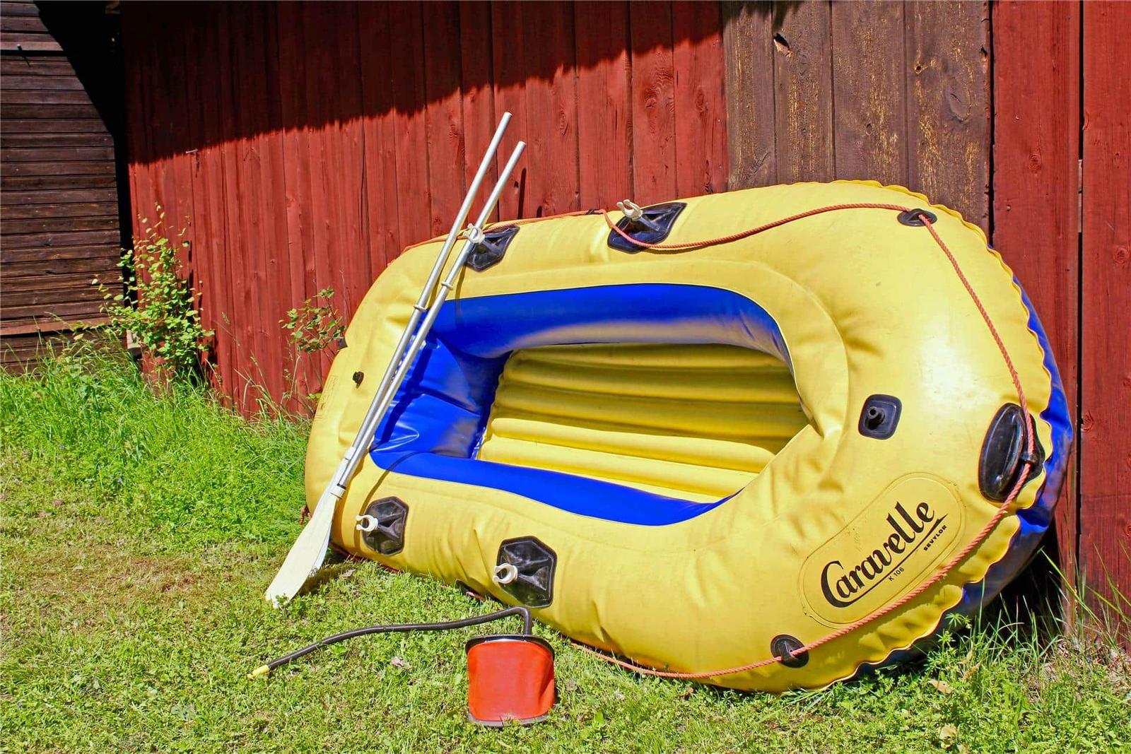 Yellow inflatable boat with oar and pump on grass near wooden wall