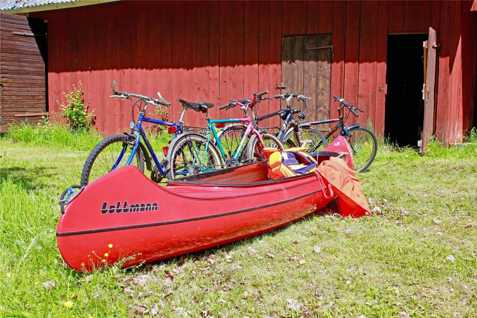 Red canoe and bicycles in front of red wooden shed on grass