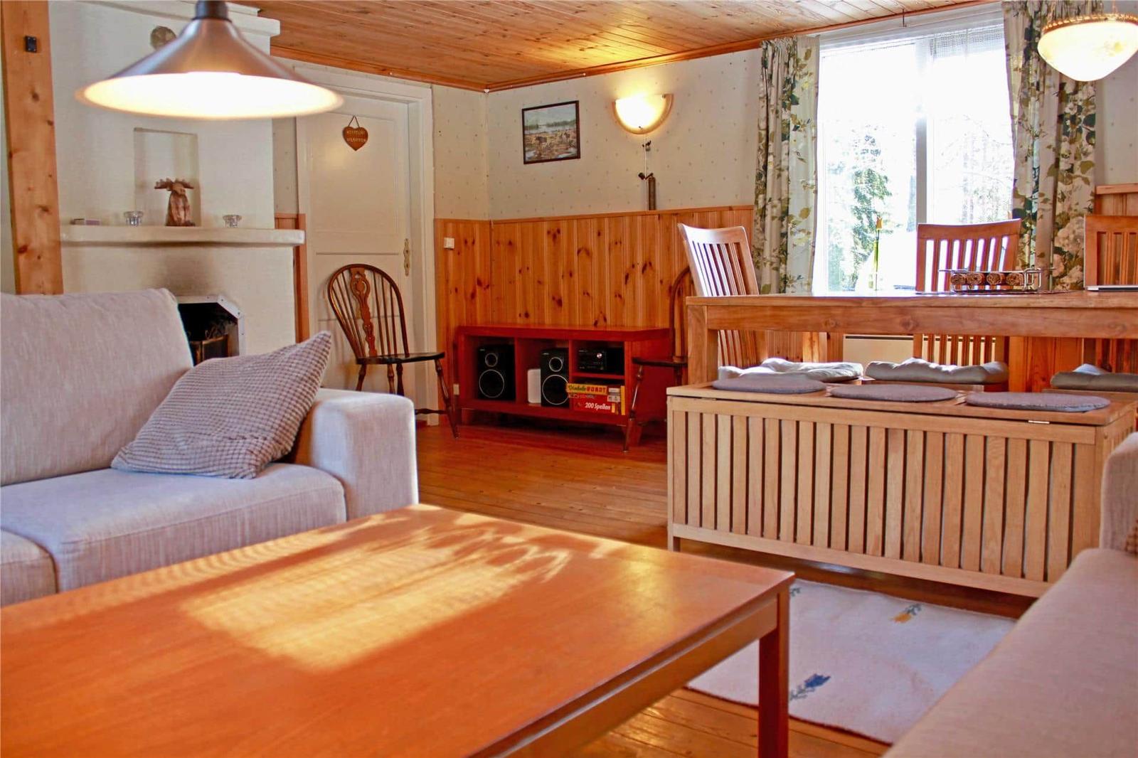 Living room with sofa, coffee table, and dining table. Wooden walls and window with curtains.