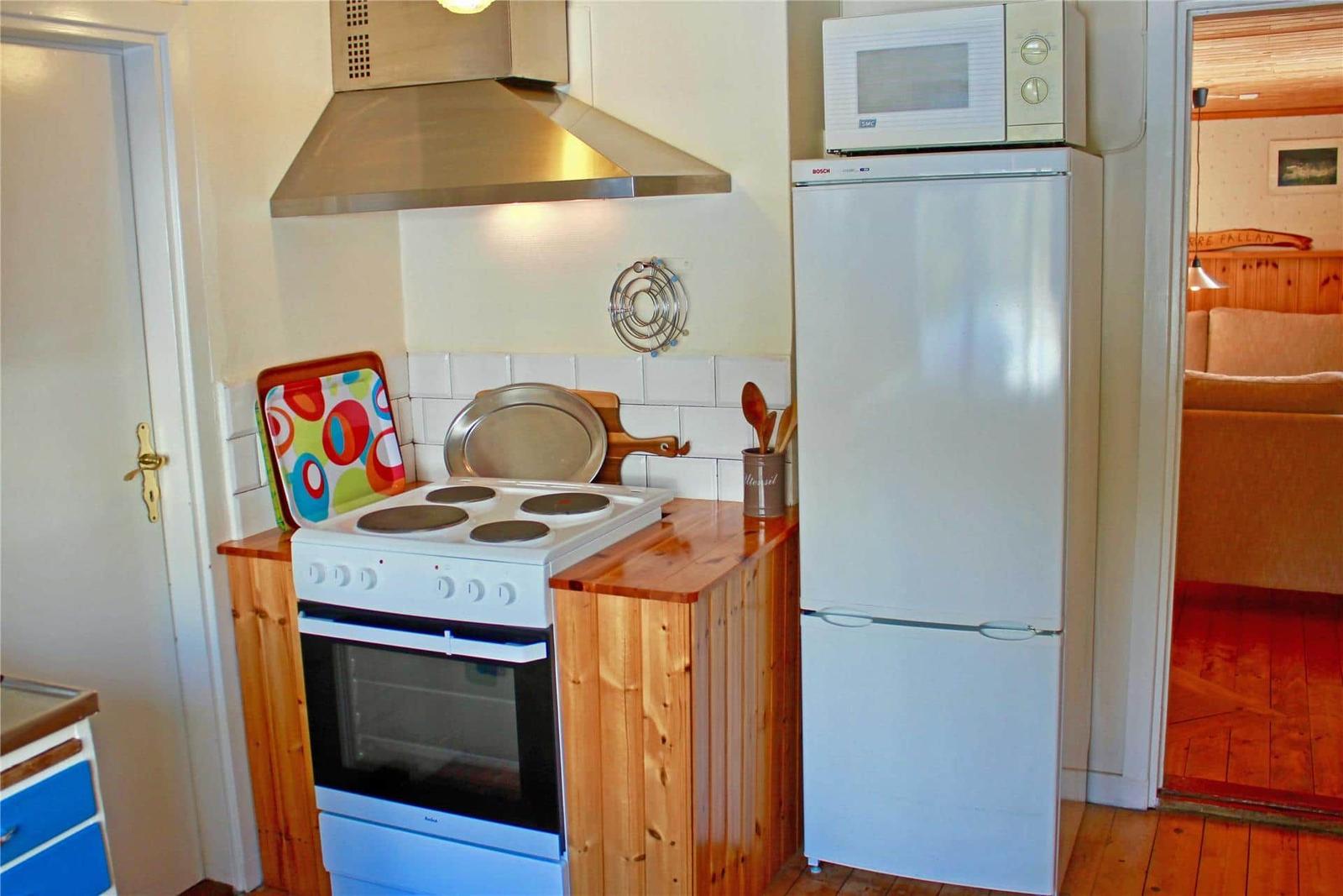 Kitchen with stove, refrigerator, and microwave. Wooden surfaces and white tiles.