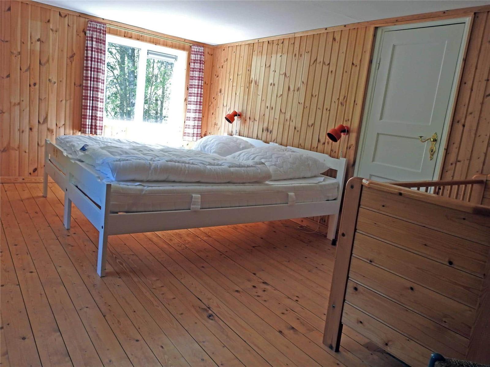 Bedroom with wooden walls, white bed, and window with view of forest.