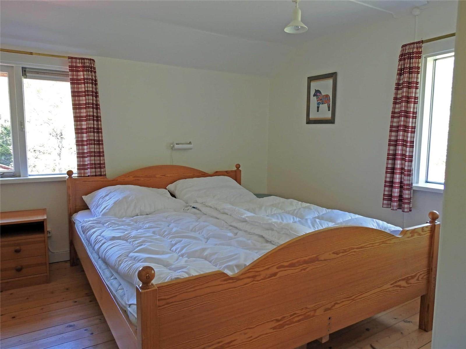 Double bed with white bedding, wooden floor, and two windows with red curtains.