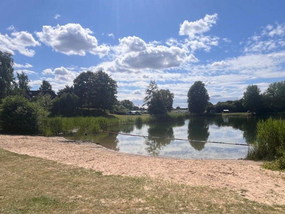 Sonniger Tag am See mit Sandstrand und grüner Umgebung.