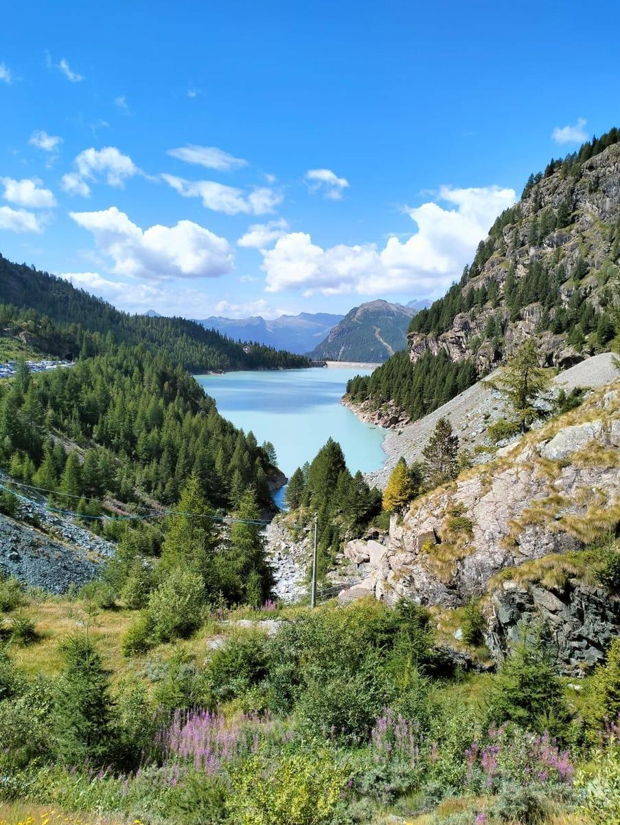 Ein See liegt in einer tiefen Schlucht zwischen bewaldeten Bergen unter blauem Himmel.