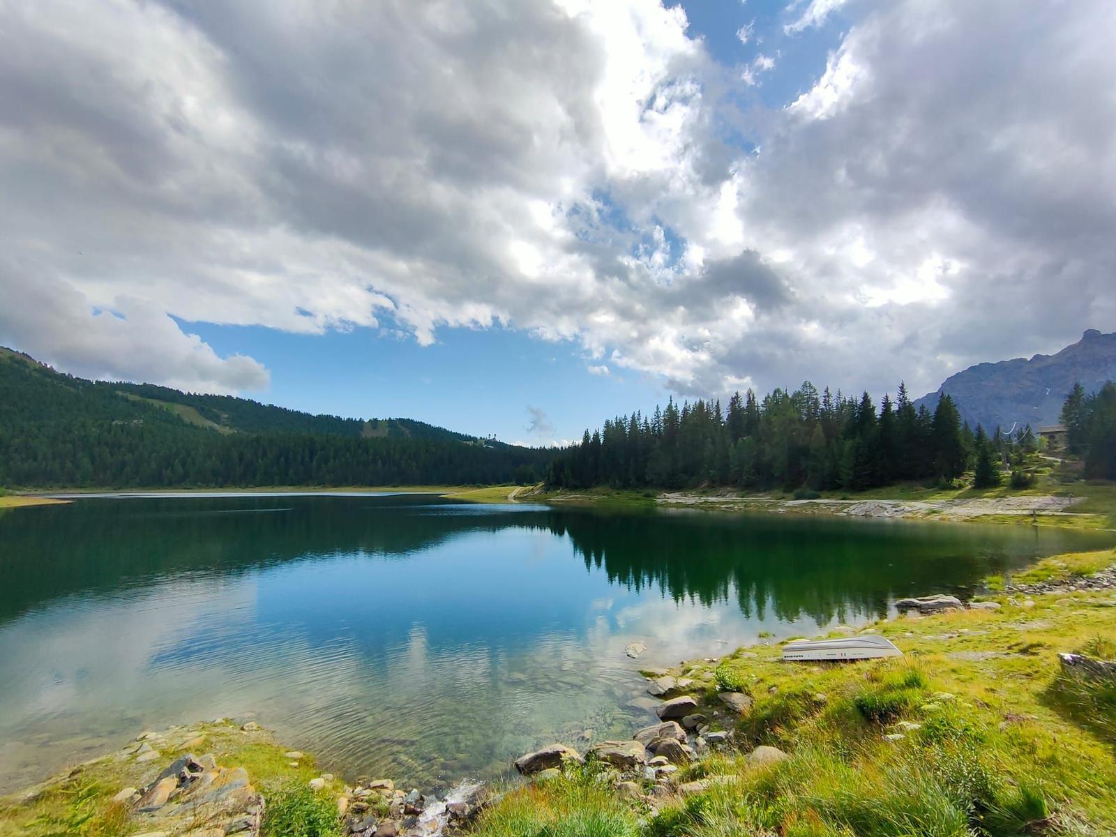 Ein ruhiger See mit grüner Umgebung und Bergen im Hintergrund.