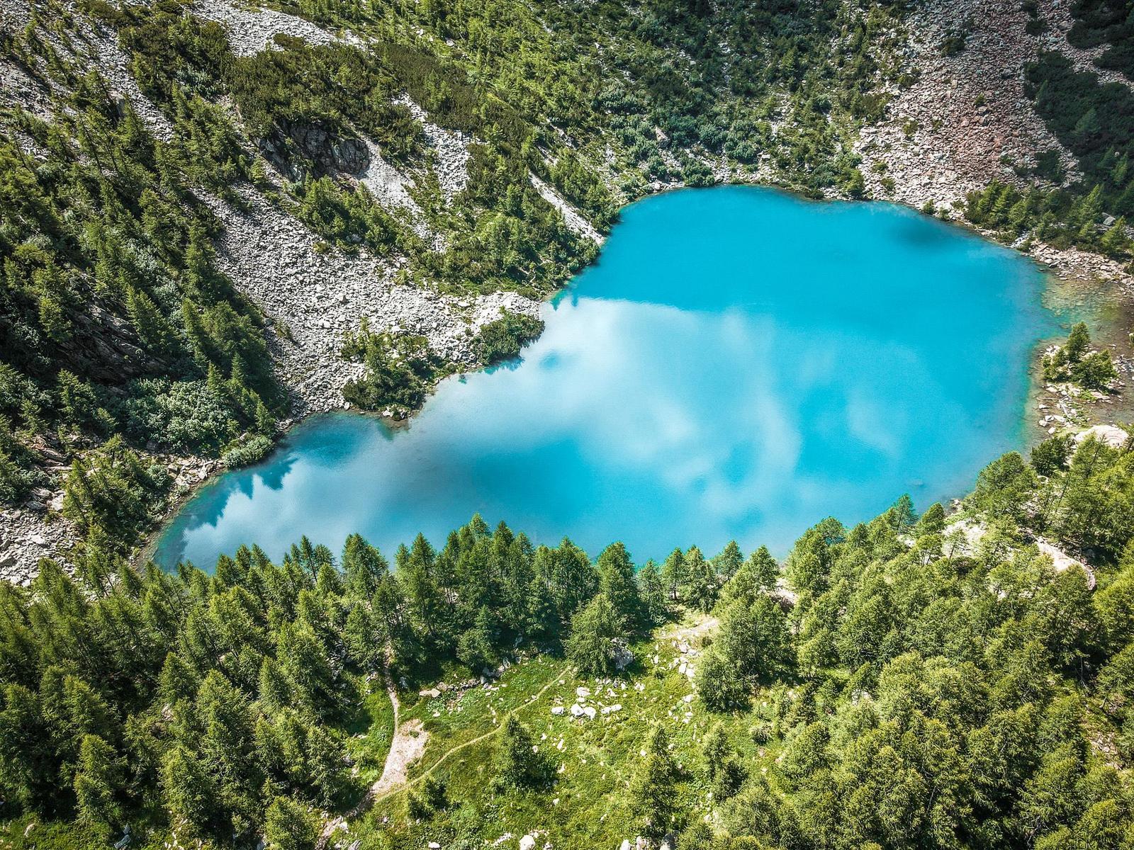 Ein tiefblauer See inmitten von grünen Wäldern und steinigem Gelände.