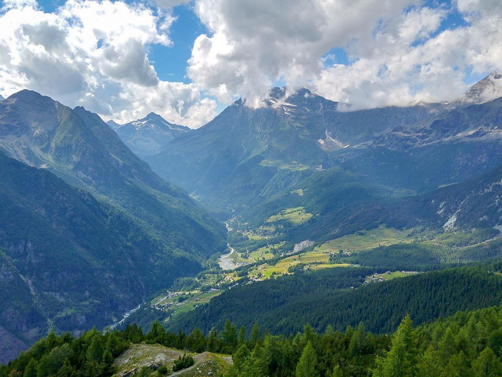 Panoramablick auf einen tiefen Tal mit Bergen und grünen Wäldern unter blauem Himmel mit Wolken.