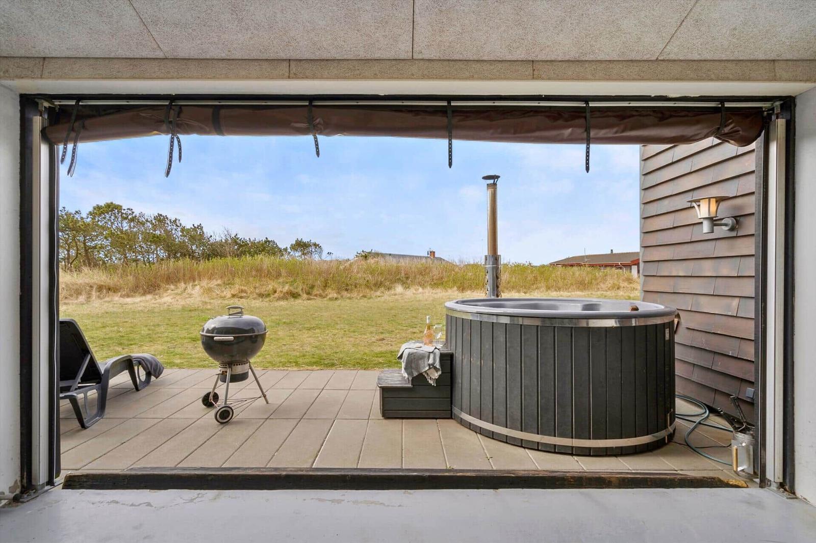 Terrasse mit Whirlpool, Grill und Liegestuhl. Blick auf Grasland und Himmel.