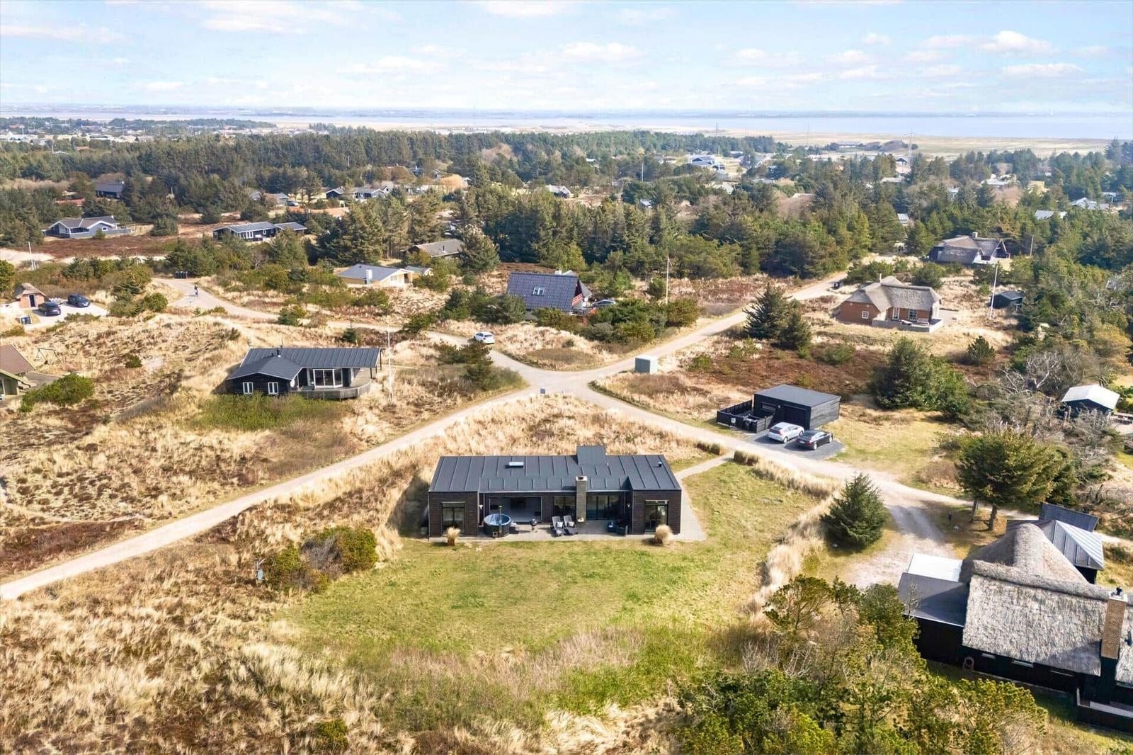 Modernes Haus mit Whirlpool auf grünem Grundstück. Umgeben von Wald und Dünen.