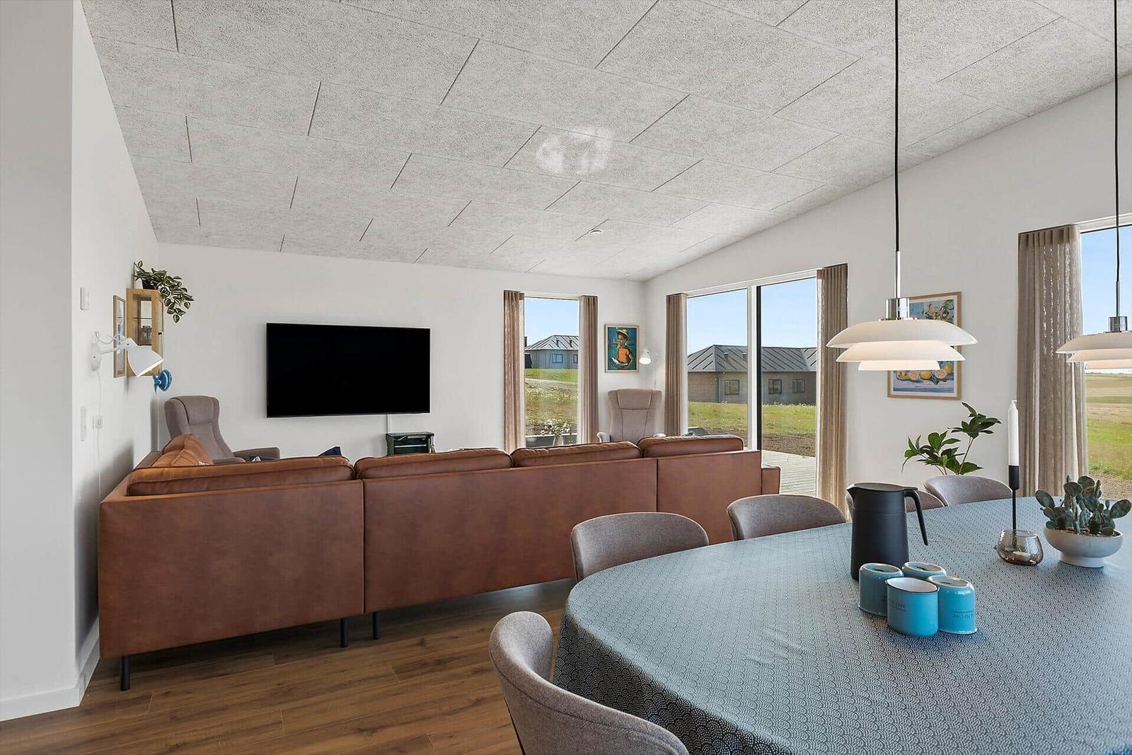 Wohn- und Essbereich mit braunem Sofa, runder Tisch und großen Fenstern.