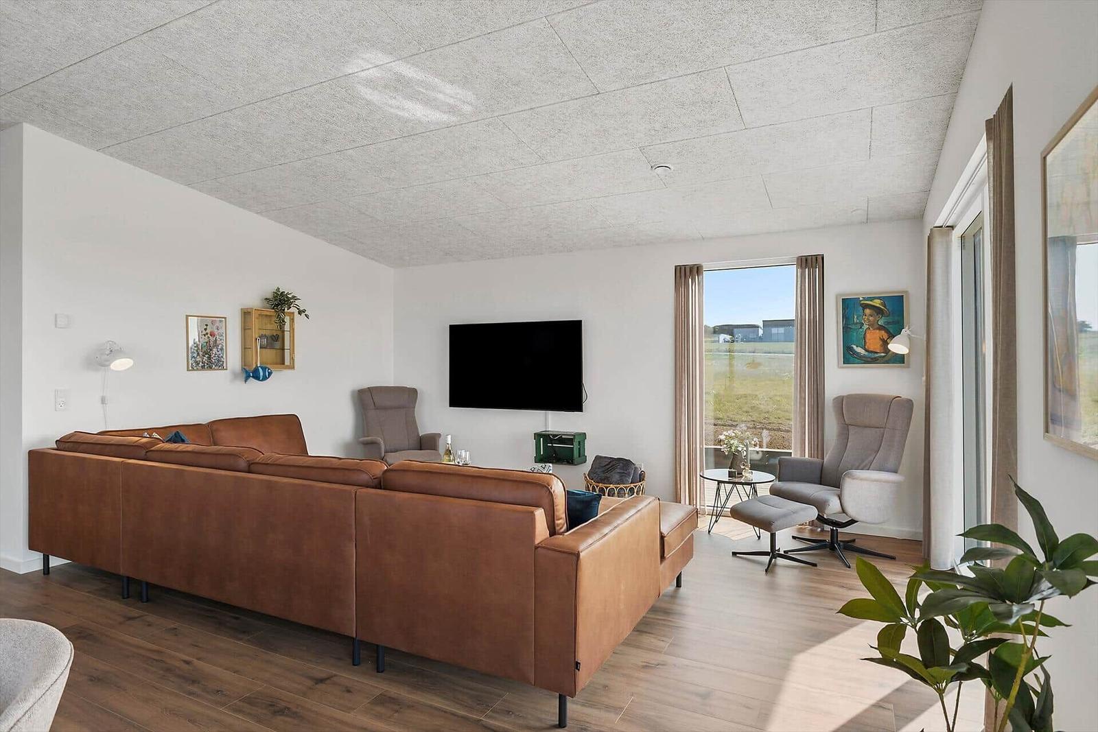 Wohnzimmer mit braunem Sofa, Fernseher und Sicht auf Grünland.