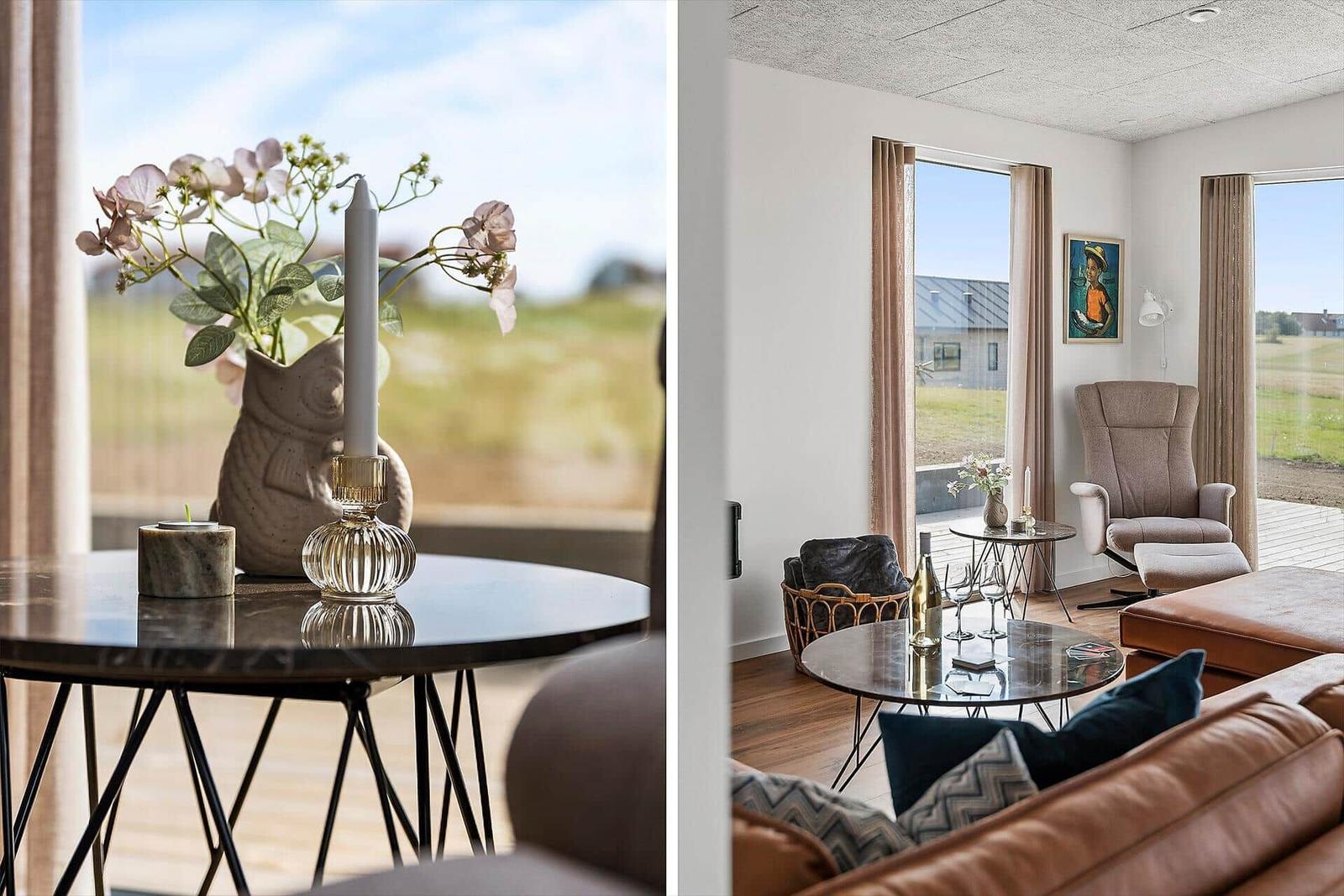 Ein Wohnzimmer mit braunen Sesseln, runden Tischen und großen Fenstern mit Blick auf Felder.