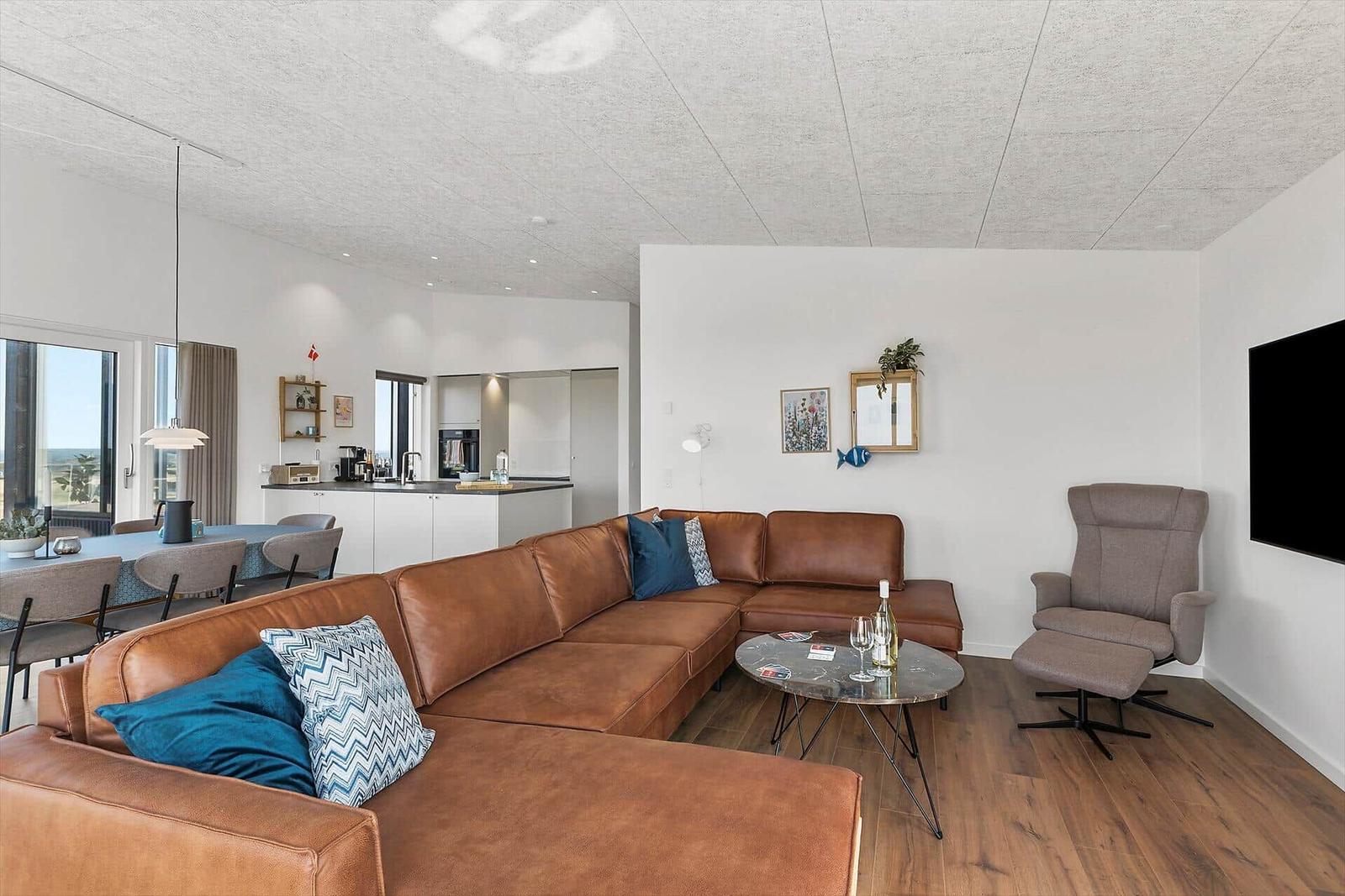 Wohnzimmer mit braunem Sofa, Esstisch und Küche im Hintergrund.