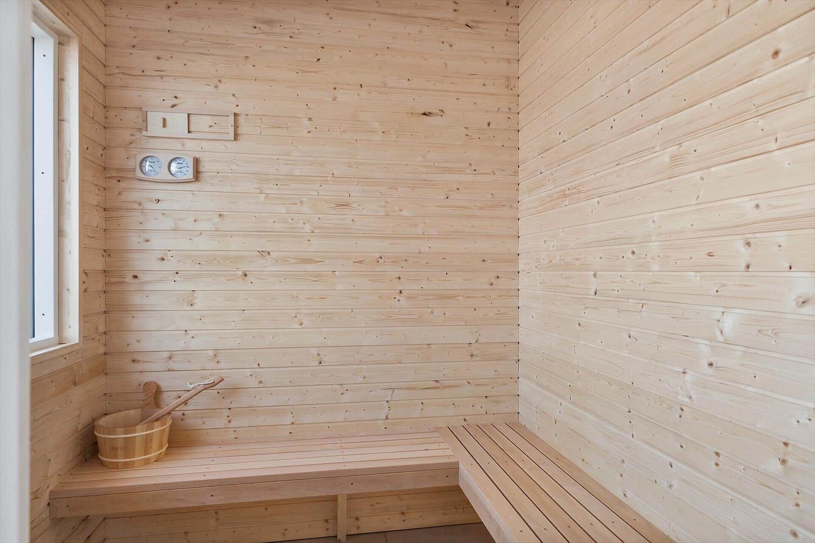 Sauna mit Holzwand, Sitzbank und Eimer mit Löffel.