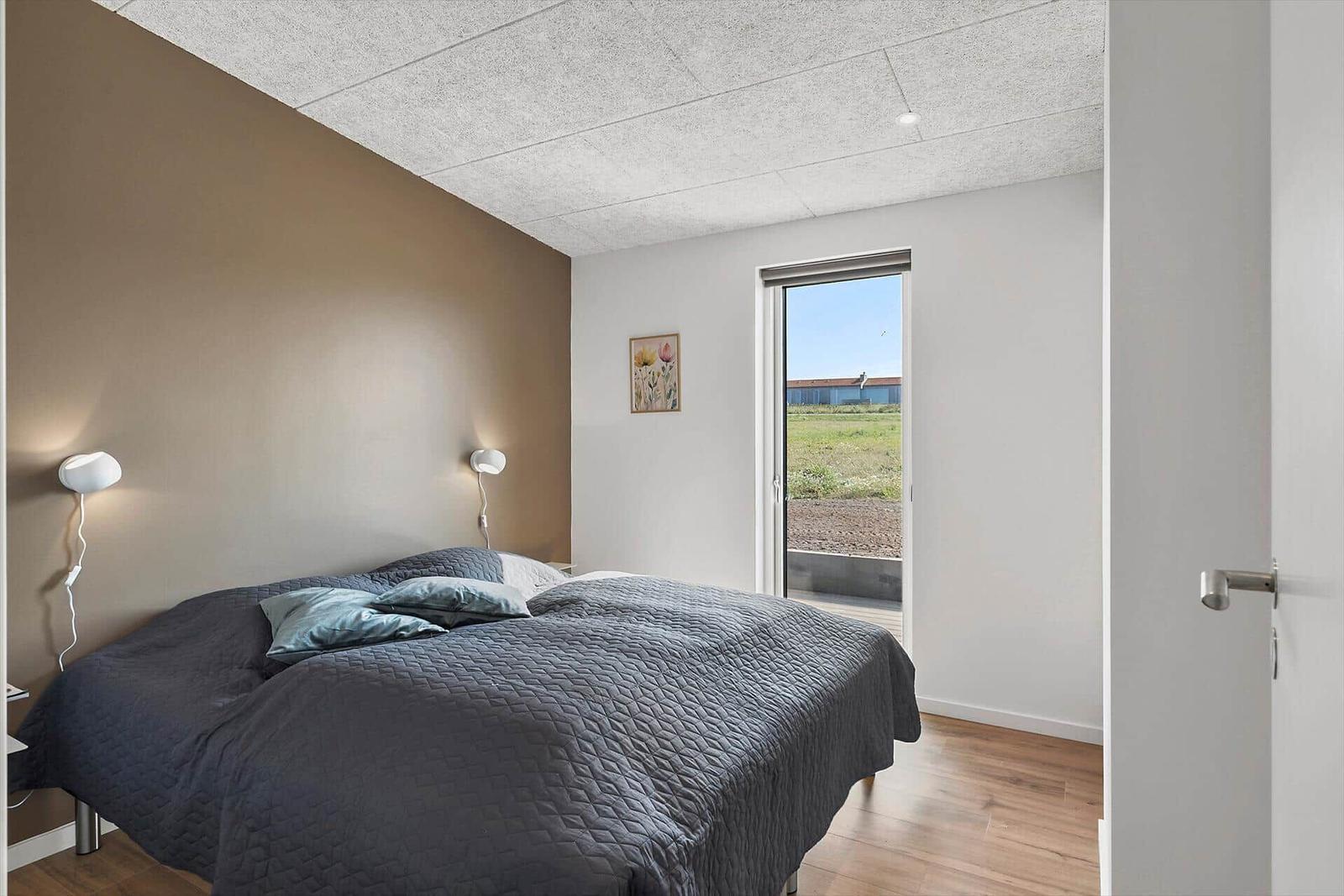 Schlafzimmer mit Bett, Wandlampen und Fensterblick auf Feld.