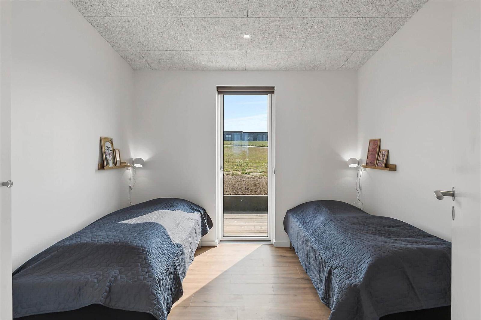 Zwei Betten mit dunkelblauen Bettdecken stehen in einem Raum mit Holzboden und Fenster zur Außenseite.