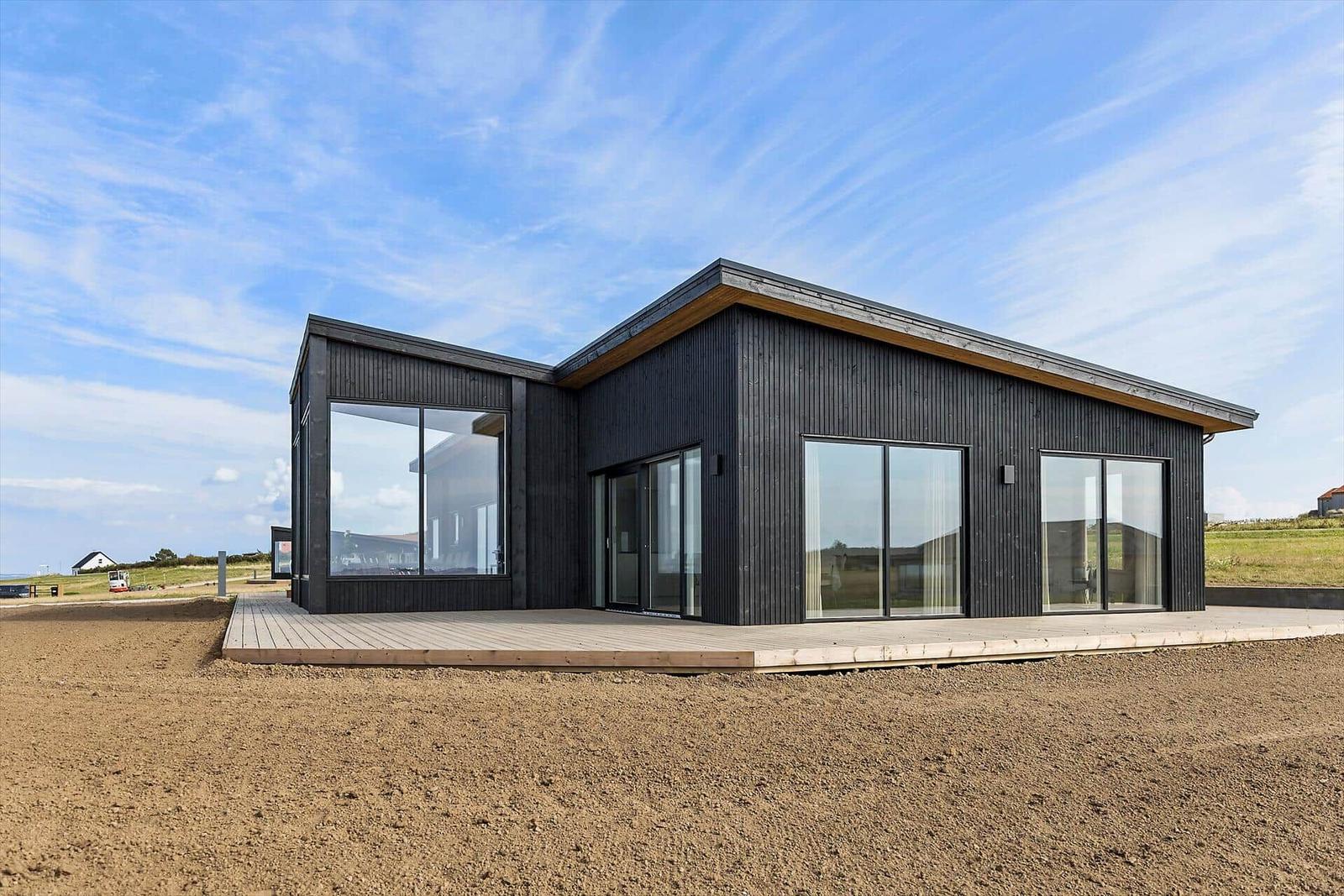 Moderne Villa mit großzügigen Glasflächen und Holzterrasse im Freien.