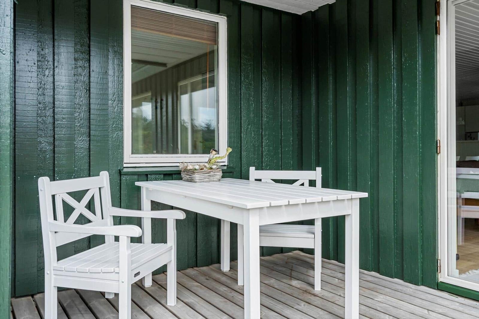 Weiße Terrassenmöbel vor grünem Holzhaus mit Fenster und Glastür.