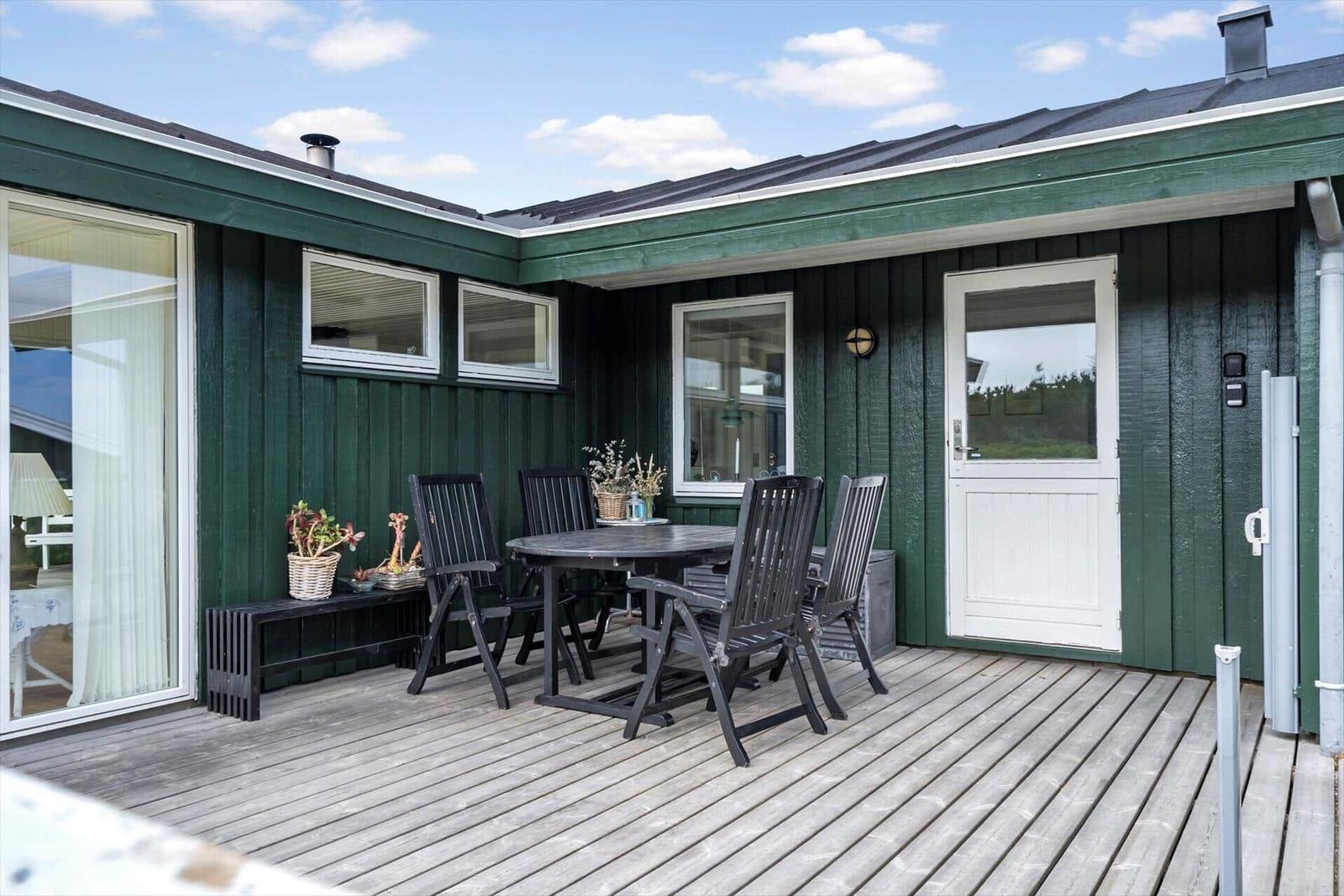 Terrasse mit Tisch, Stühlen und Pflanzen an grünem Haus