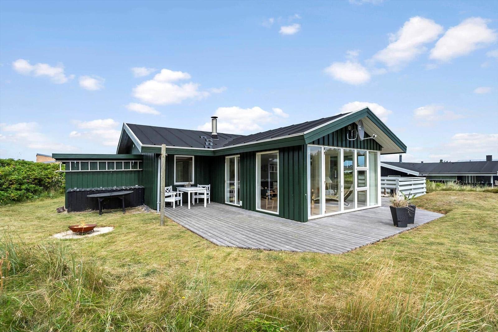Grünes Ferienhaus mit Terrasse, Grill und Sitzgelegenheiten im Freien.