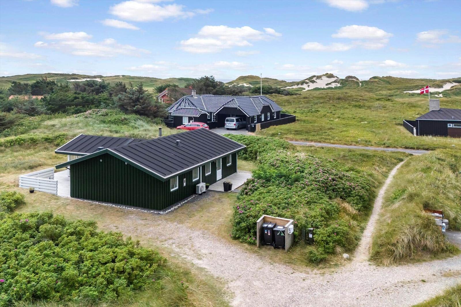 Ein grünes Haus mit Dach und Terrasse steht auf einer grünen Wiese.