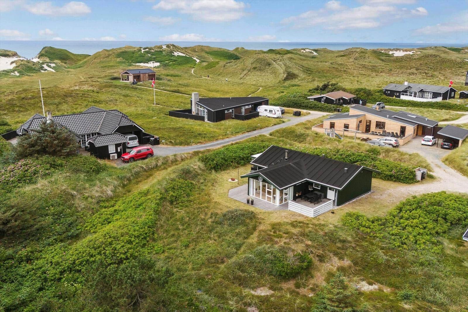 Häuser auf grünen Dünen mit Blick aufs Meer.