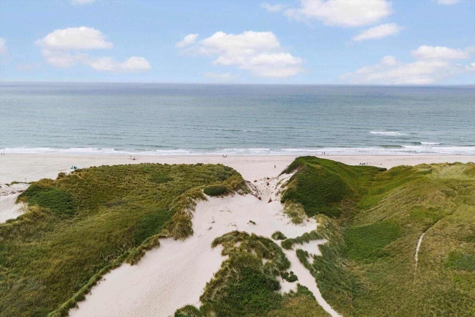 Strand mit Dünen und Meer unter blauem Himmel mit weißen Wolken.