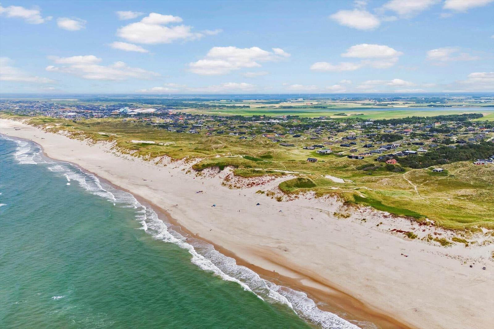 Strand mit Dünen und Häusern am Meer unter blauem Himmel.