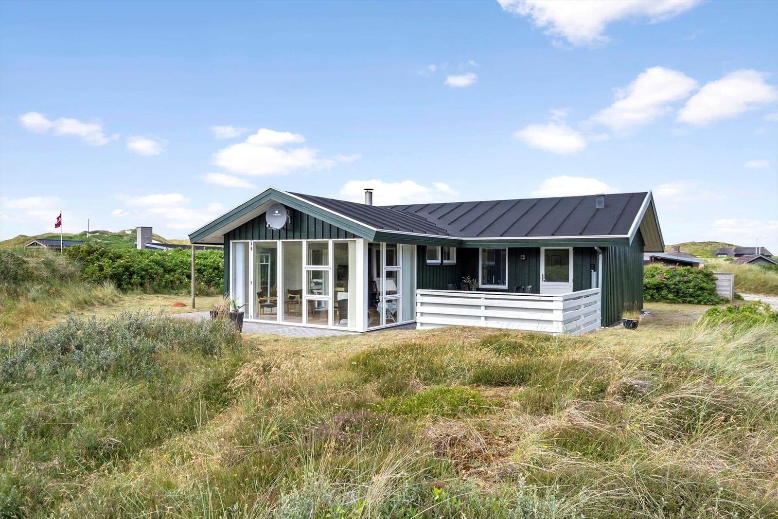 Ein Haus mit grünem Holz und weißer Veranda steht in einer grasbewachsenen Landschaft.