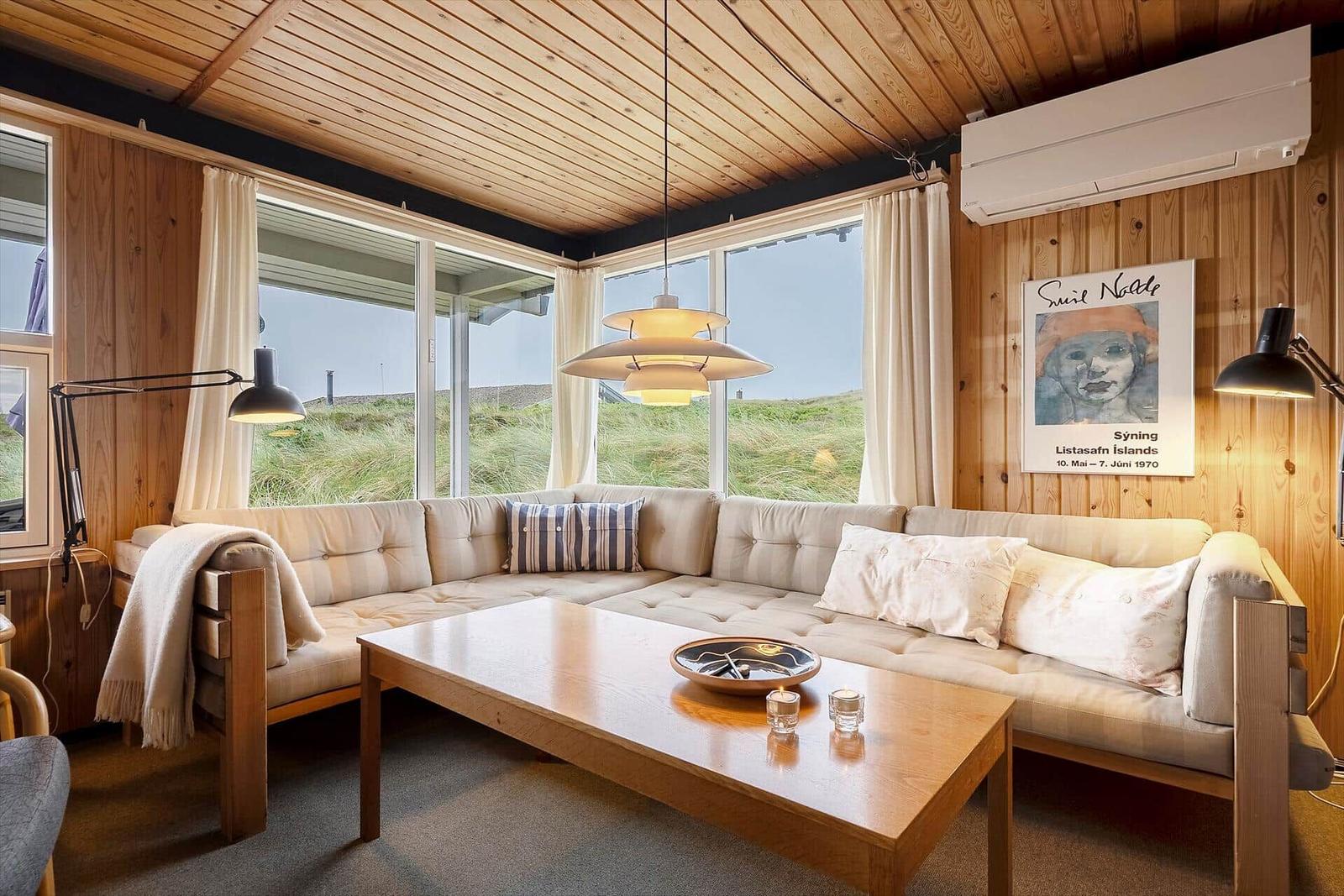 Wohnzimmer mit Sofa, Tisch und großen Fenstern. Holzwände und Decke.