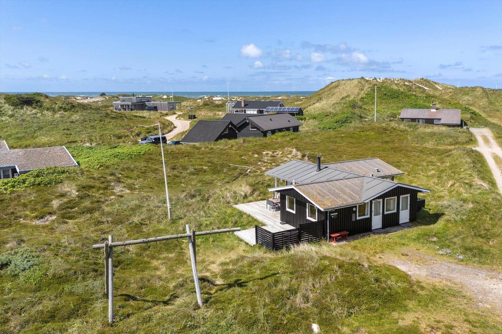 Holzhütte auf Dünen mit Blick aufs Meer und Windkraftanlagen.