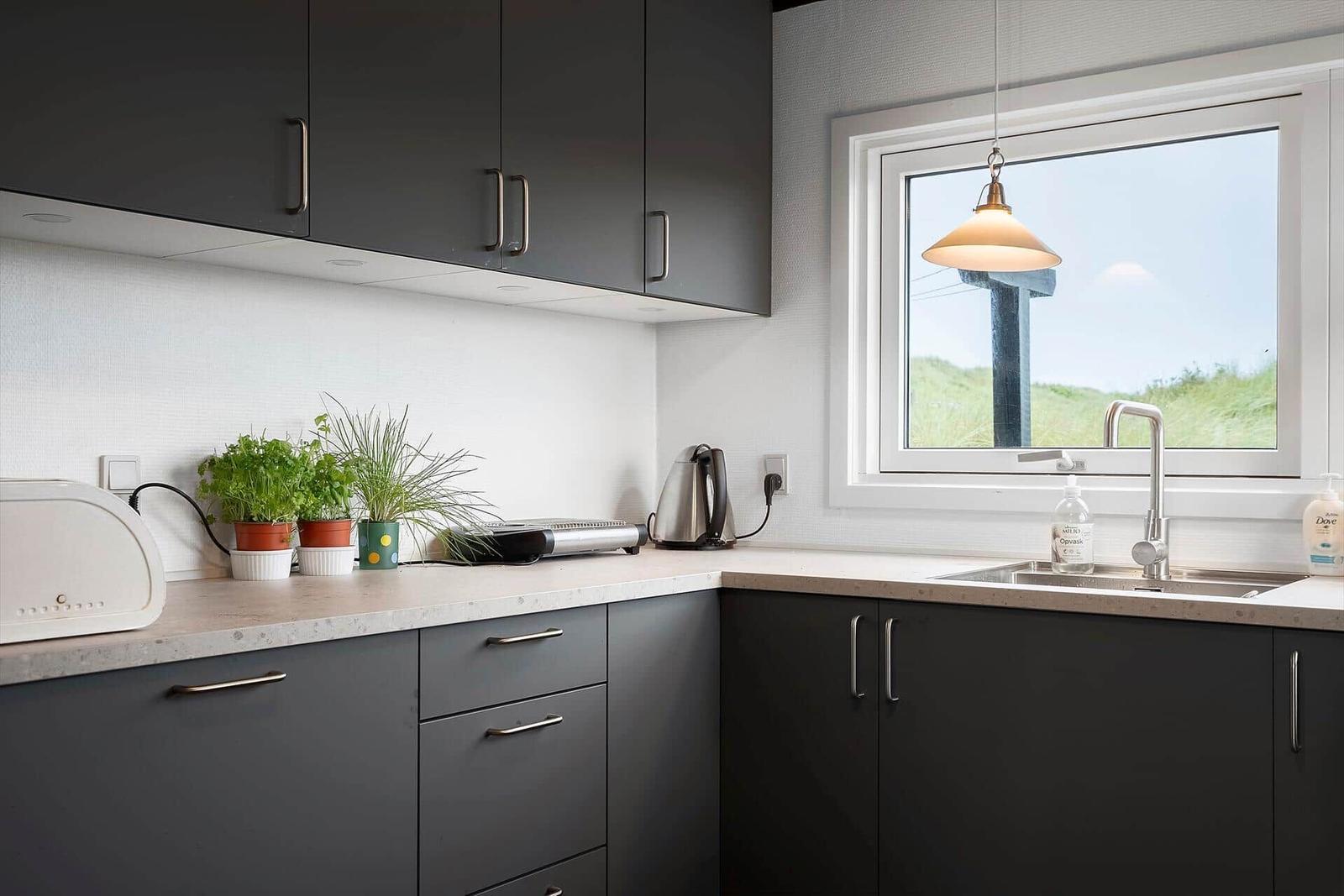 Küche mit dunklen Schränken, Arbeitsplatte und Fenster mit Blick auf Gras.