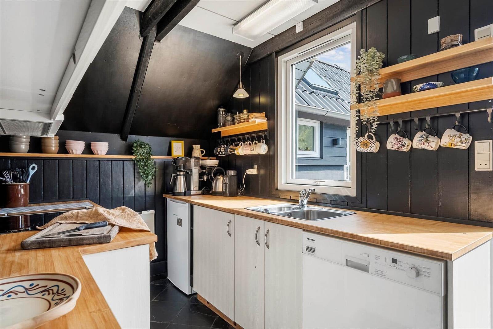 Kitchen with wooden surfaces, black walls, and window view.