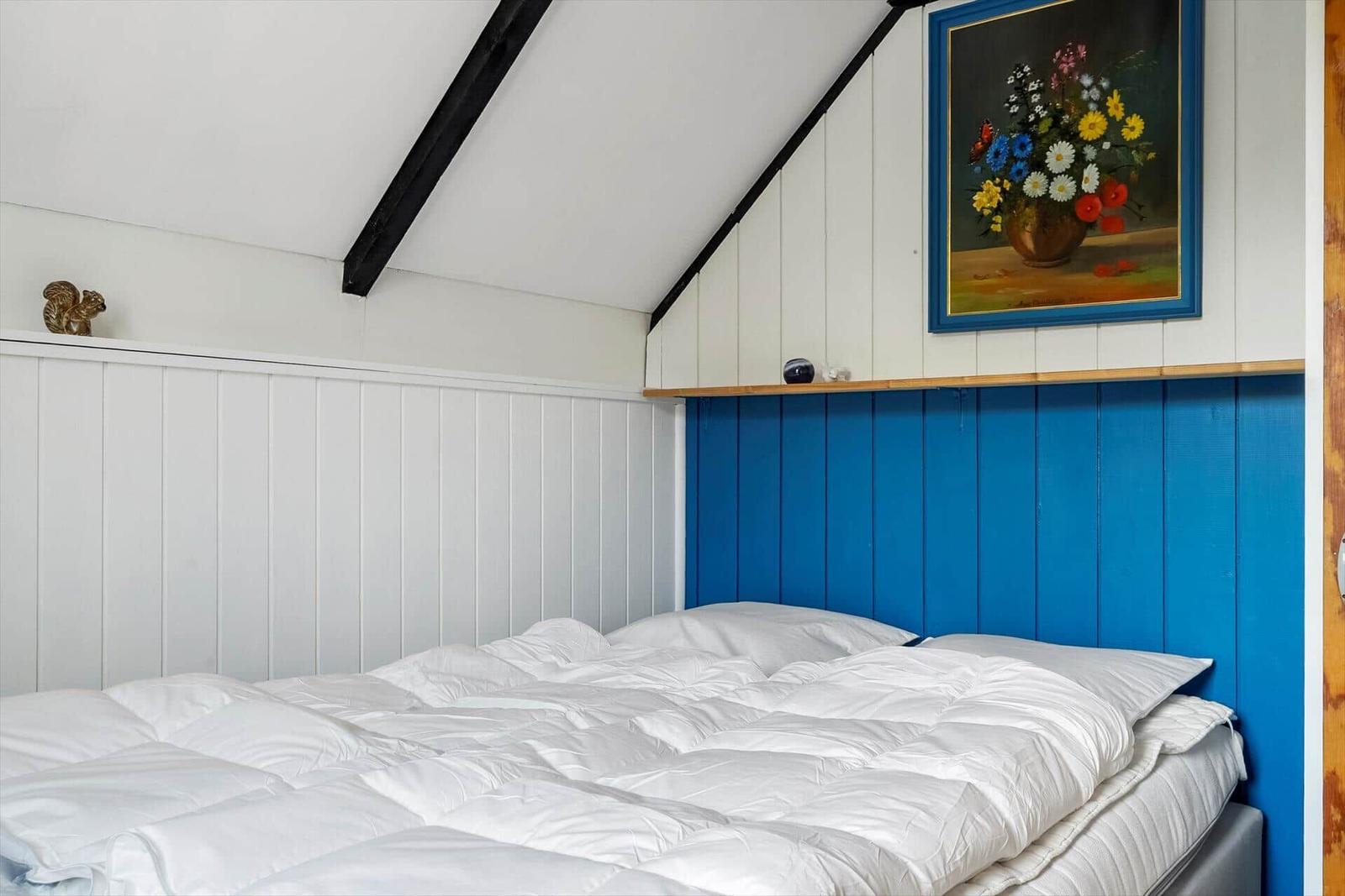 Bedroom with bed, blue wall, and painting on the wall.