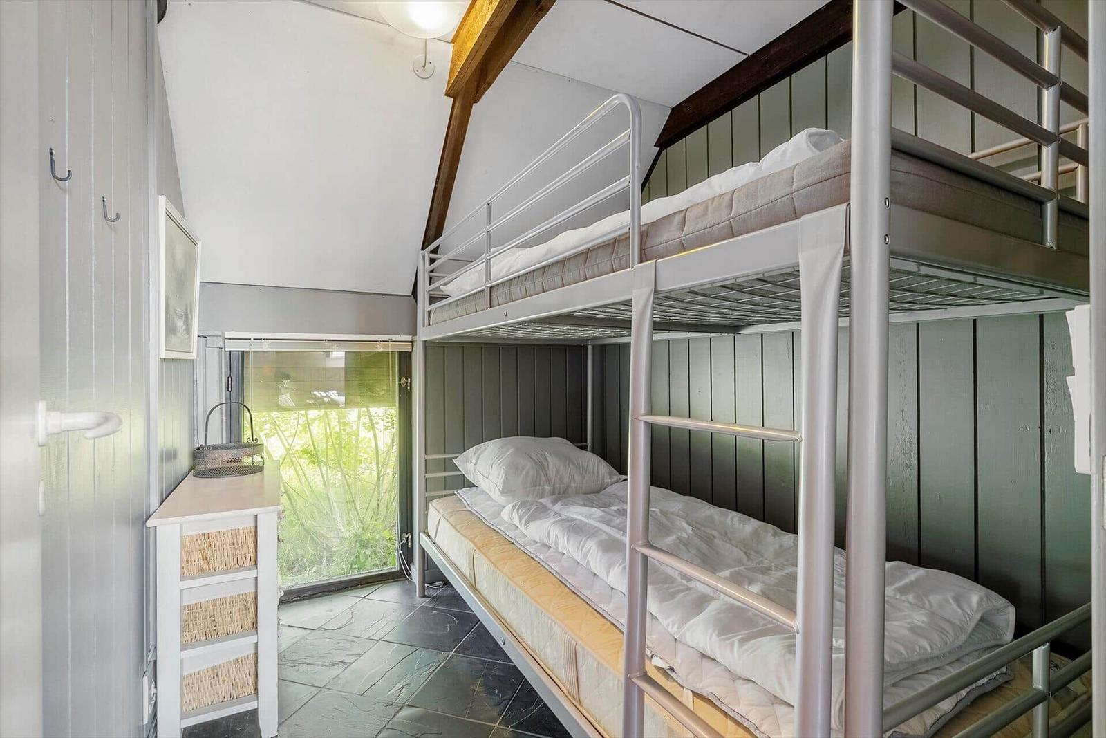 Room with bunk bed, window and small dresser.