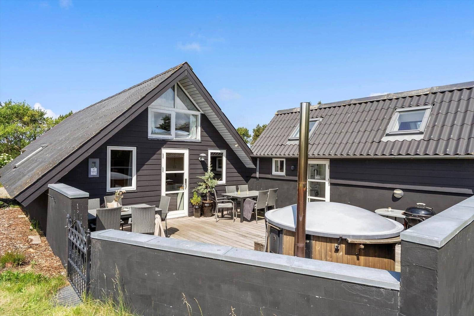 Modern house with terrace, hot tub, and grill. Black siding, wooden deck, and clear view.