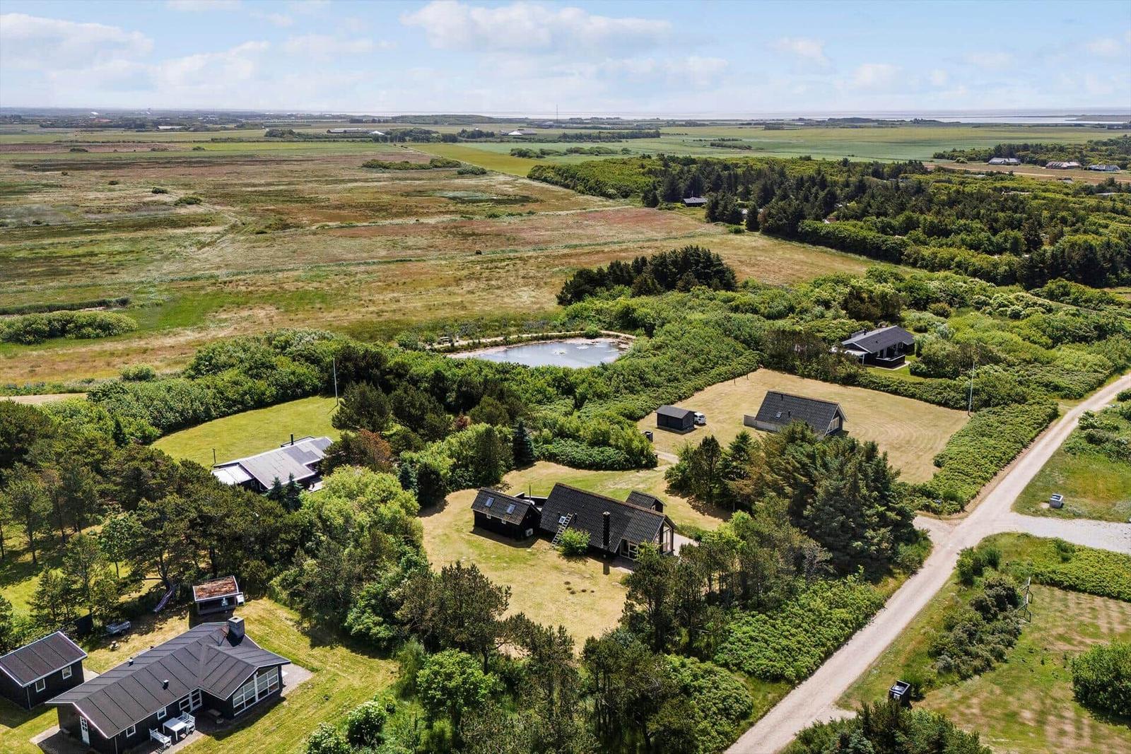 Aerial view of several cabins surrounded by greenery and open fields near a pond.