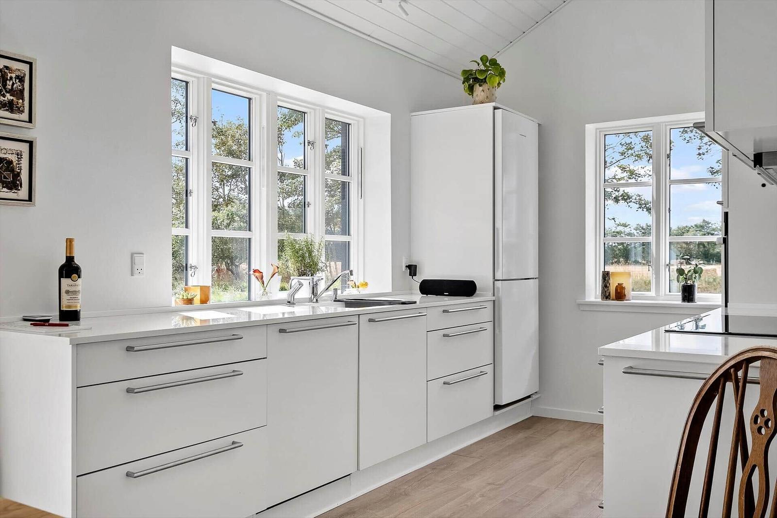 Küche mit weißen Schränken, Fenstern und Holzboden. Auf der Arbeitsplatte steht eine Weinflasche.