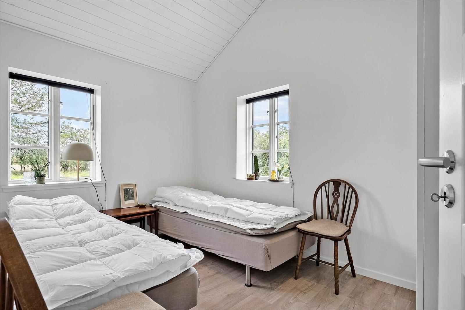 Zwei Betten, zwei Fenster, Stuhl und Holzboden im Schlafzimmer.