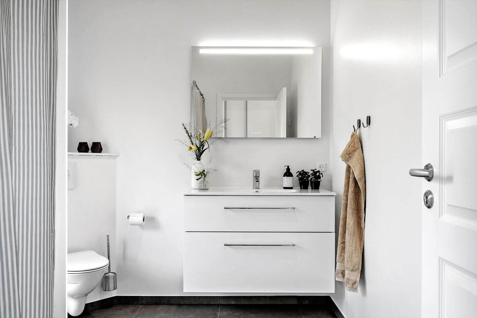 Badezimmer mit Waschbecken, Spiegel und Toilette. Handtuch hängt an Wand.