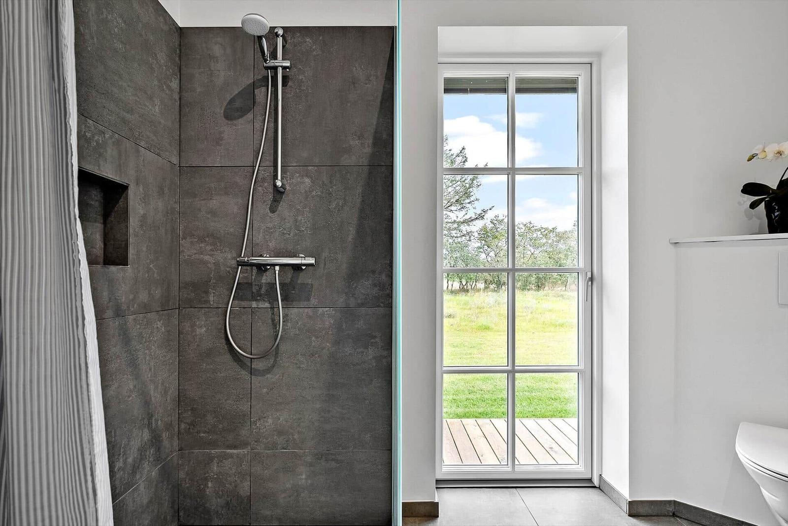 Duschkabine mit dunklen Fliesen und Fenster zum Garten.